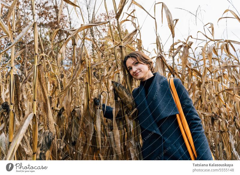Woman hugging dry corn stalks in cornfield in autumn woman coat rows fall outdoors rural countryside harvest seasonal agricultural farming nature autumnal