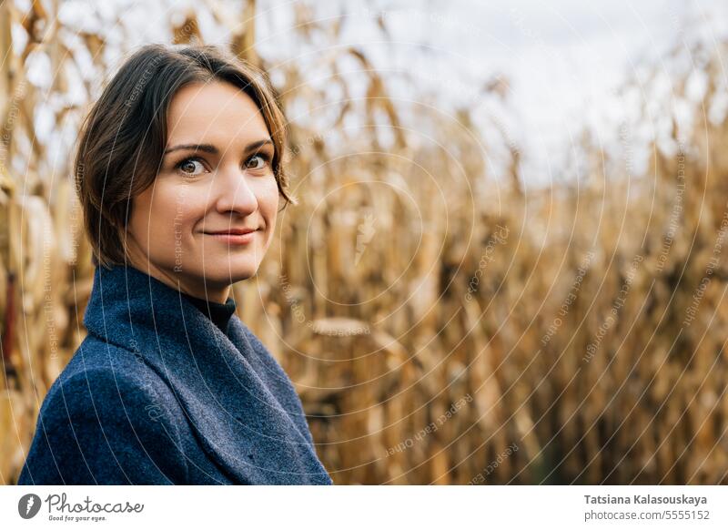 Portrait of confident smiling young short-haired woman in autumn in the middle of a cornfield portrait smile coat rows fall outdoors rural countryside harvest