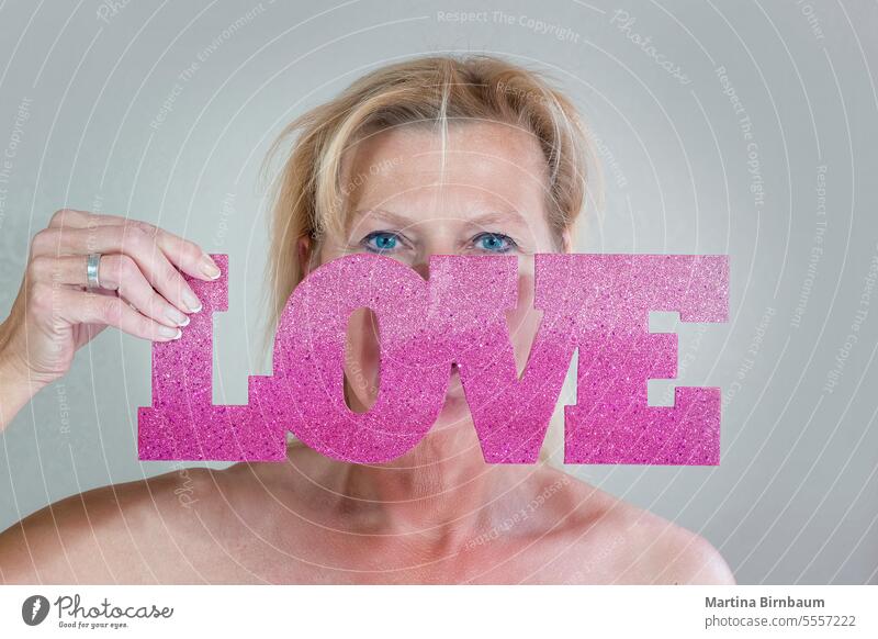Blonde smiling caucasian woman holding a sign saying love in front of her face romantic girl attractive beautiful letters studio shot signs symbols young adult