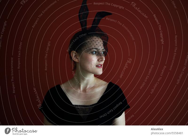 Young woman with a black top, lace veil and black lace bunny ears stands in front of a red wall and looks to the side Woman Hare ears Vail Point portrait pretty