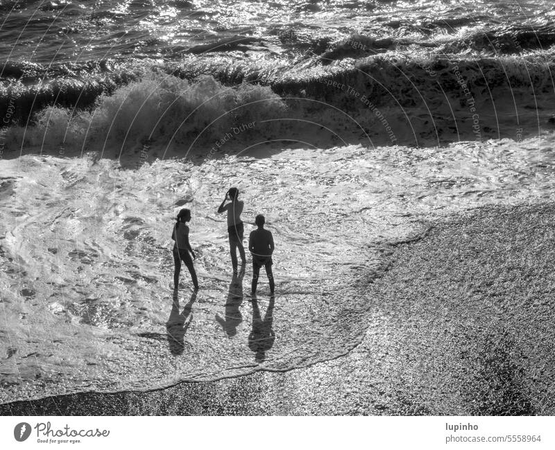 Three children standing in the surf three Surf White crest Back-light black-and-white from above Foam wave Autumn Ocean vacation coast Liguria Shadow