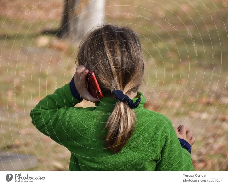 girl with blonde hair and ponytail playing with mobile phone. playing outdoors child kid smartphone internet device online young using game little happy