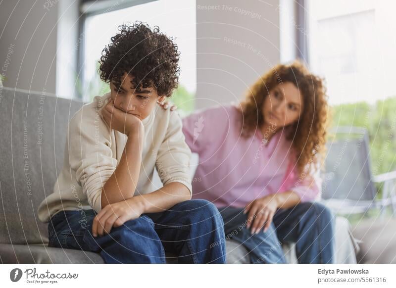 Mother comforting her son on sofa in living room at home real people adult apartment bonding boy child family female indoors kid lifestyle love mom mom and son
