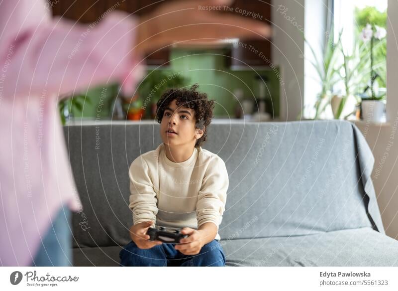 Teenage boy playing video games while his mother is not happy about it real people adult apartment bonding child family female home indoors kid lifestyle love