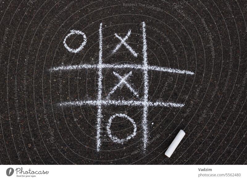 Tic-tac-toe game drawn with white chalk on asphalt.  Drawing on the pavement. Chalk crayons street childhood day circle cross shape choice victory activity