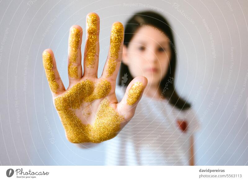 Serious young girl showing her palm hand covered of golden glitter while doing stop sign micro plastic microplastics gesture problem ban prohibition expression