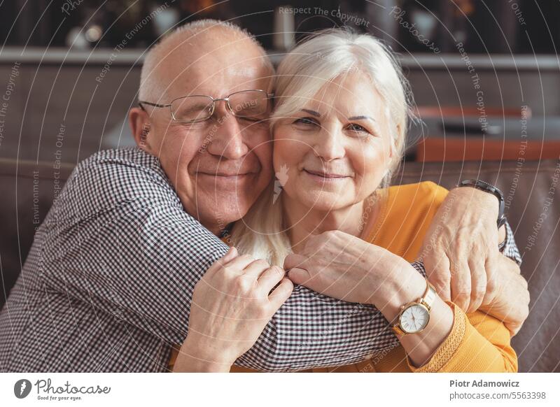 Cheerful senior couple hugging on sofa at home cheerful man retirement love woman embracing kiss blond lucky carrying content pension couch elderly envelope