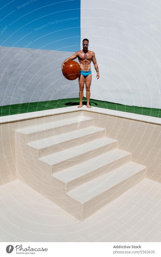Man with fitness ball standing on poolside man exercise shirtless workout empty summer male naked torso muscular barefoot bare shoulders activity sportsman