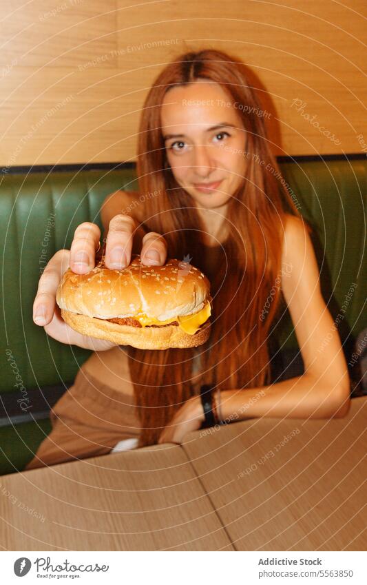 Young woman showing hamburger girl eat fast food young table sitting one dinner lunch snack holding hand unhealthy nutrition indoors restaurant redhead red hair