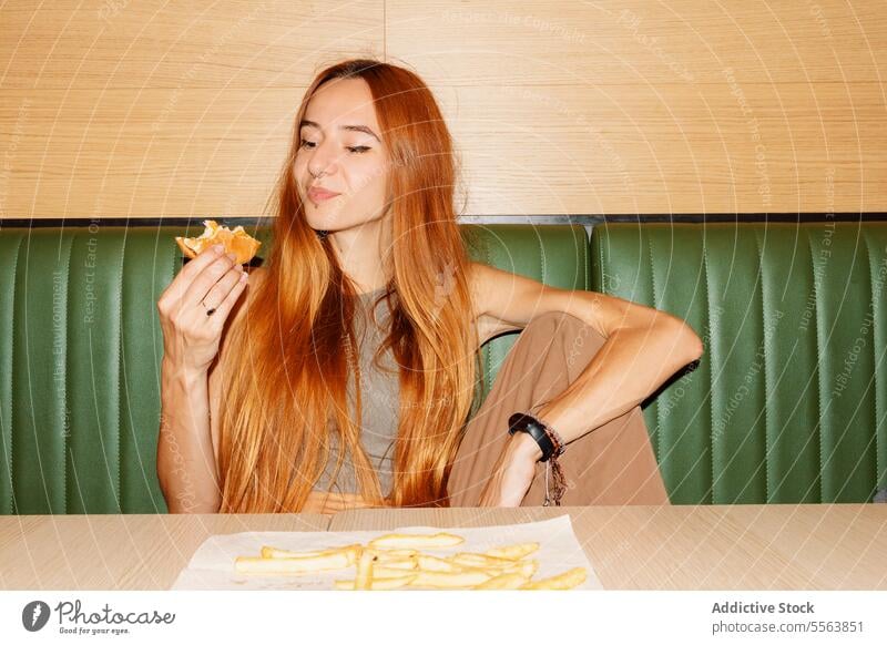 Young woman enjoy eating hamburger girl fast food young table sitting one dinner lunch snack holding hand unhealthy nutrition indoors restaurant redhead