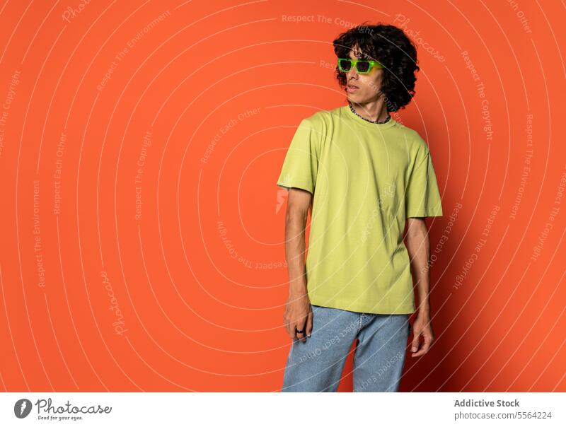 Confident young ethnic man in sunglasses standing near turquoise backdrop funky dancer fashion curly hair cool individuality male latin american hispanic style