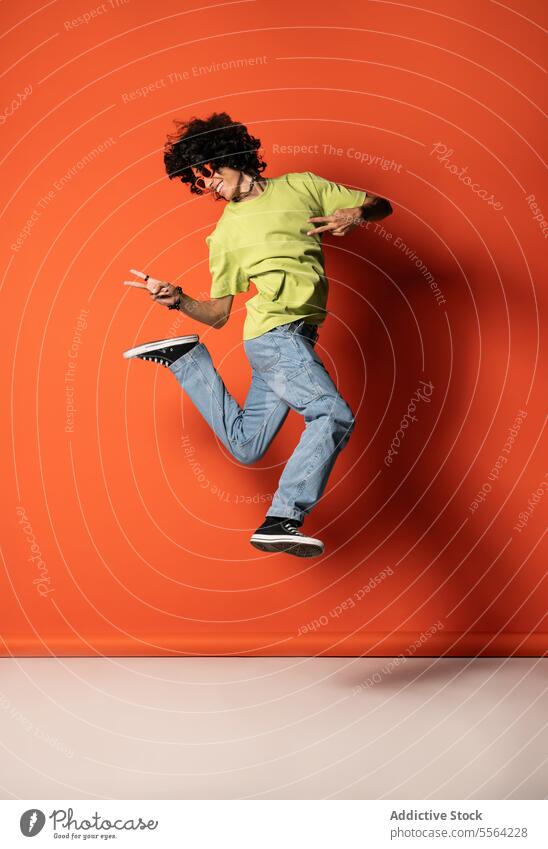 Happy young ethnic man with curly hair dancing against pink wall in light jump dance funky flexible dancer victory balance perform male stand latin american