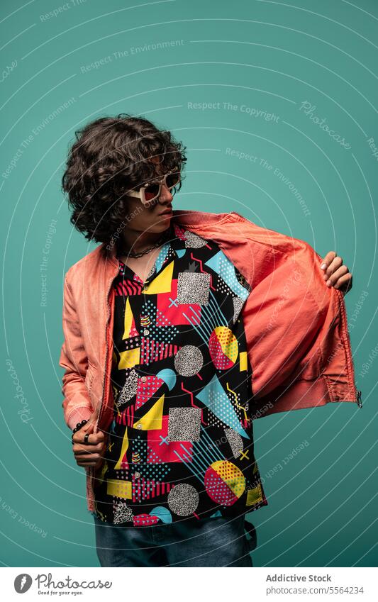 Happy young ethnic man with pink jacket standing at turquoise backdrop funky smile happy show flap sunglasses shirt male latin american hispanic demonstrate