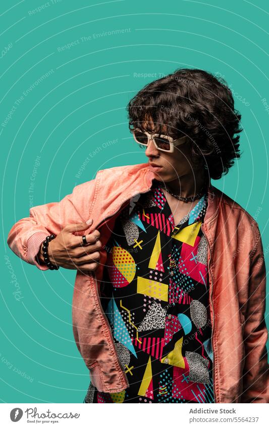 Happy young ethnic man with pink jacket standing at turquoise backdrop funky smile happy show flap sunglasses shirt male latin american hispanic demonstrate