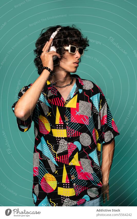 Young ethnic man with headphones enjoying music against turquoise backdrop listen funky cool male young style latin american hispanic device gadget sunglasses