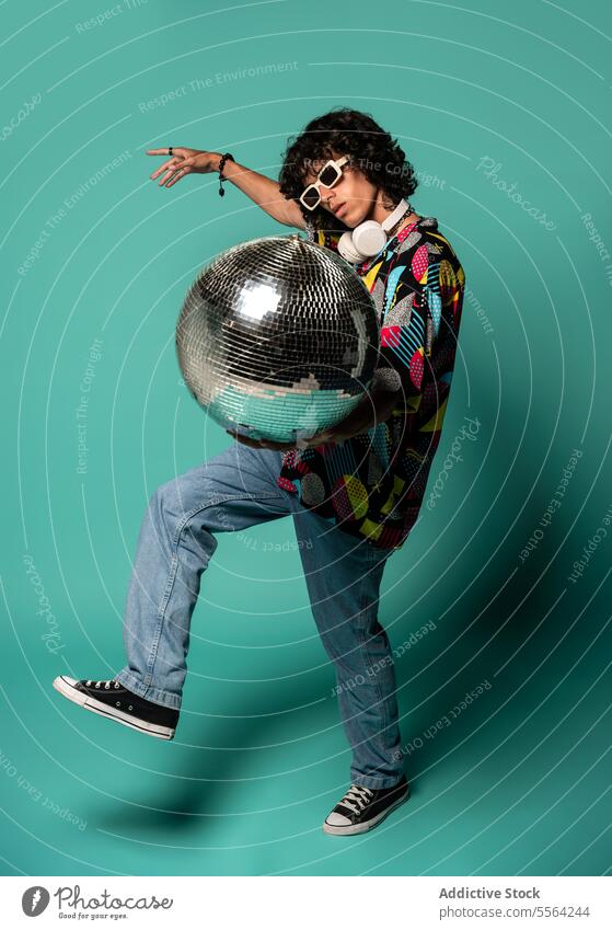 Syncopated young ethnic man dancing with disco ball with hand and leg raised sunglasses show colorful gesture shirt funky fashion male stand latin american