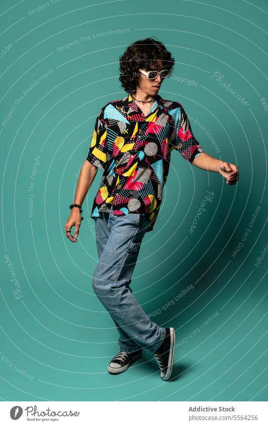 Stylish young ethnic man dancing with moving legs and arms near turquoise wall funky dancer perform excited move energy sunglasses male sit latin american