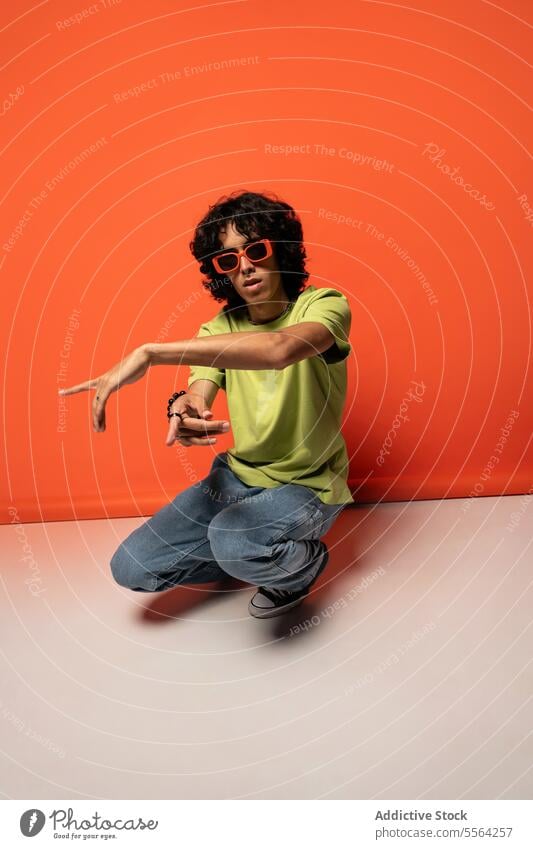 Young ethnic man dancing with sunglasses near red wall dancer excited expressive funky having fun enjoy male young stand latin american hispanic style move