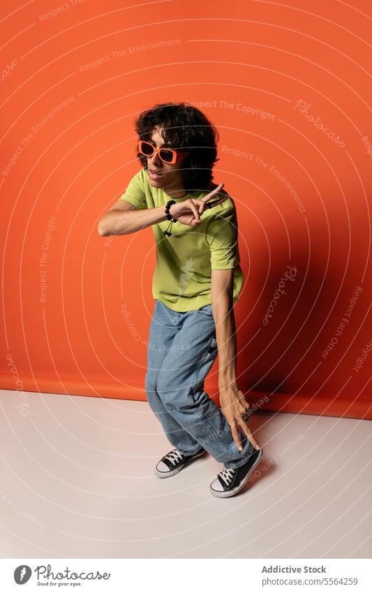 Young ethnic man dancing with sunglasses near red wall dancer excited expressive funky having fun enjoy male young stand latin american hispanic style move