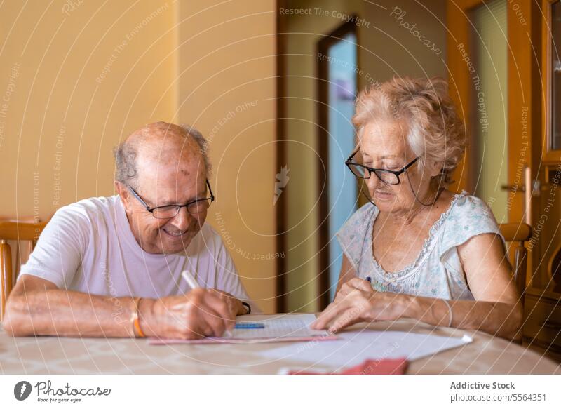 Grandparents doing memory exercises at home grandparents grandfather grandmother eyeglasses sit table chair practice focus concentrate work looking down house