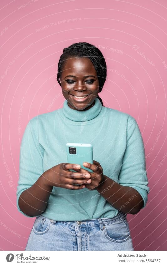 African woman smiling at her smartphone in a pink setting african teal turtleneck turquoise backdrop joy style fashion portrait technology mobile cheerful