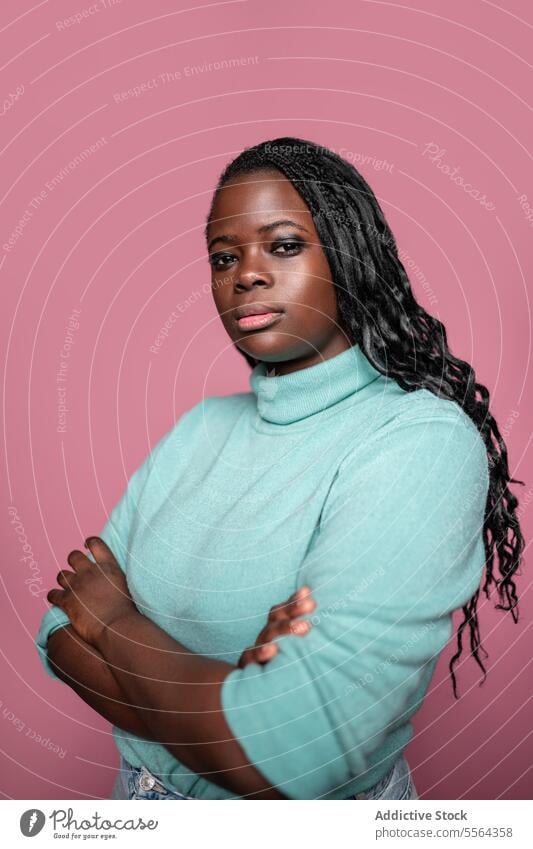 Confident African woman against pink backdrop african confidence mint green turtleneck sweater braids hair pose beauty fashion portrait stance style gaze