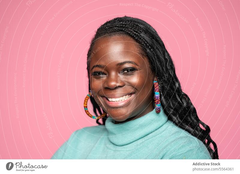 Smiling African woman with colorful earrings on pink background african smile turquoise turtleneck hoop braided hair cheerful style fashion beauty portrait