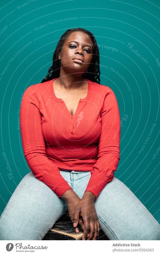 African women with confident pose against teal background african woman red blouse seated reflection thoughtful lady expression studio calm meditation casual
