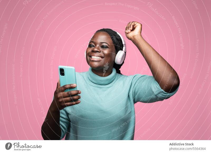 Delighted African woman with smartphone and pink headphones african smile teal delight listening background expression emotion dance vibe groove mood