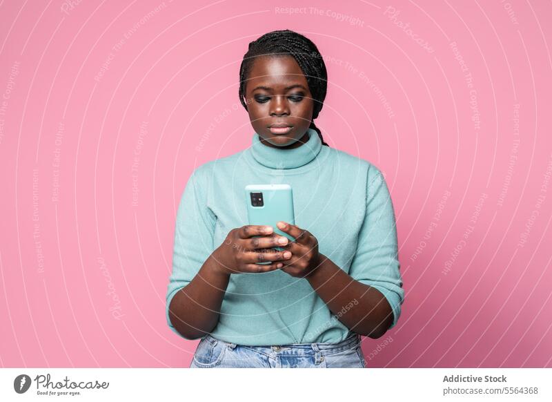 Focused african woman using phone against pink background turquoise turtleneck smartphone light blue focused young braids fashion style modern technology mobile