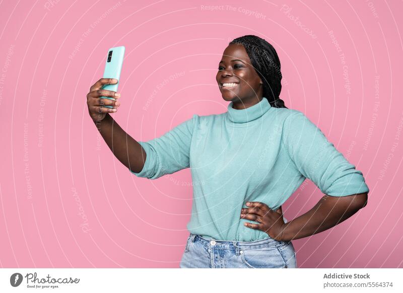 African lady captures selfie with smartphone on pink backdrop african woman teal turtleneck turquoise background joy style fashion portrait technology mobile