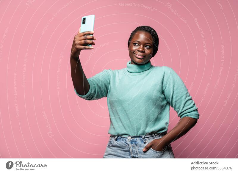 African woman taking selfie against pink background african smartphone teal sweater pose capture joy photo mobile camera fun memory lifestyle moment digital