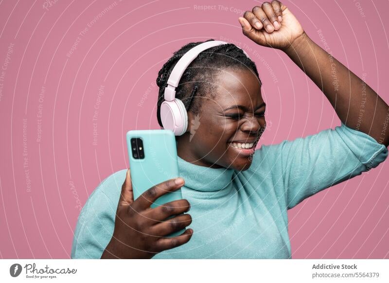 African woman enjoying music with headphones and smartphone african pink teal listening background expression emotion dance vibe groove mood entertainment