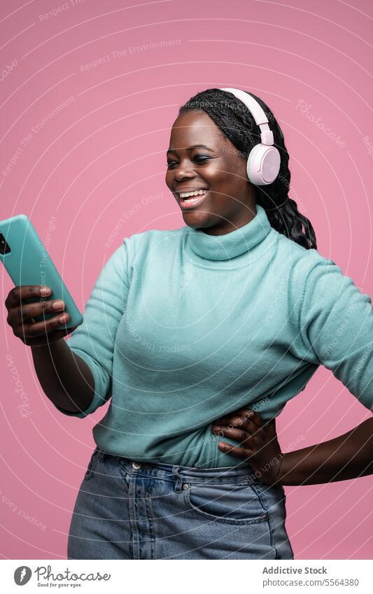 African woman enjoying music with smartphone african turquoise sweater pink headphones mint green background enjoyment fashion technology style leisure