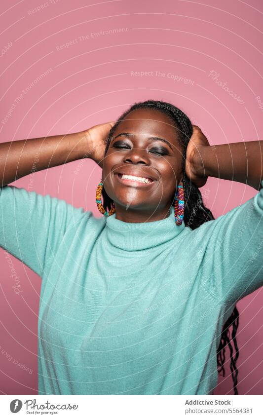 Portrait of smiling African woman with braids african portrait smile joyful happiness braided hair earrings colorful turquoise sweater pink backdrop beauty