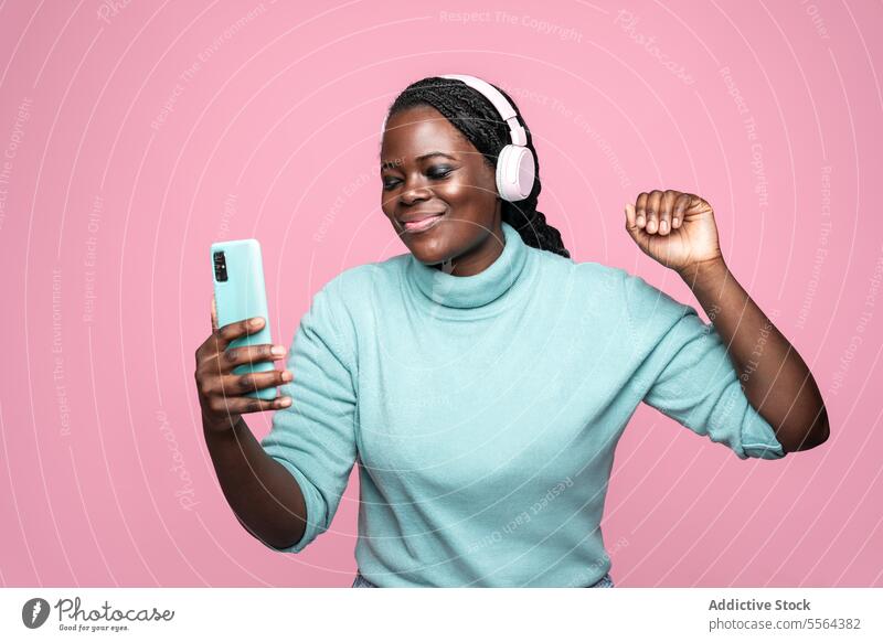 African woman enjoying music against a pink background african dance smartphone headphones backdrop rhythm fun movement groove happiness entertainment leisure