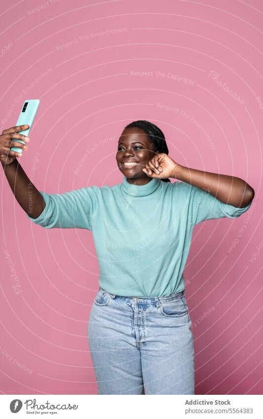 African lady captures selfie with smartphone on pink backdrop woman joy smile background pose african technology photograph mobile moment cheerful portrait