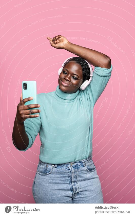 African lady captures selfie with smartphone on pink backdrop woman african headphones dance background cheerful joy mobile fun music rhythm celebrate portrait