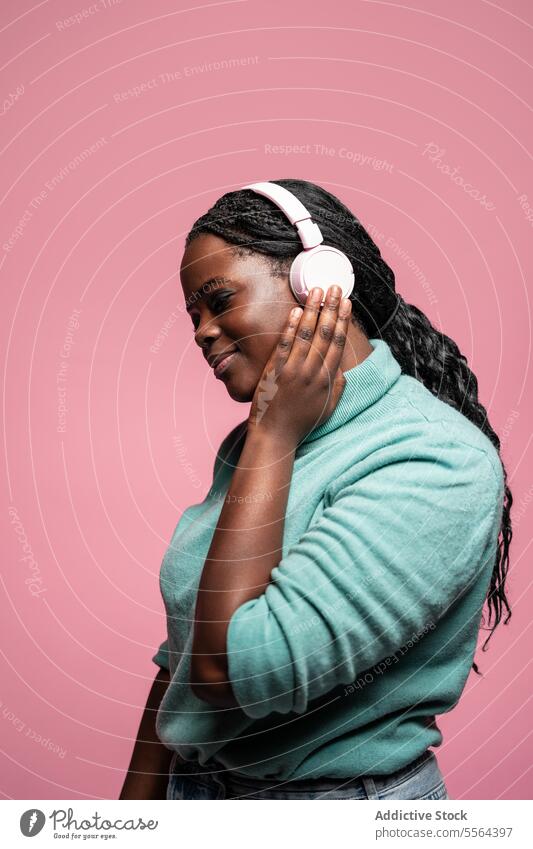 Serene african woman enjoying music headphones pink background serene listen side view calm peaceful emotion relax audio leisure sound technology melody