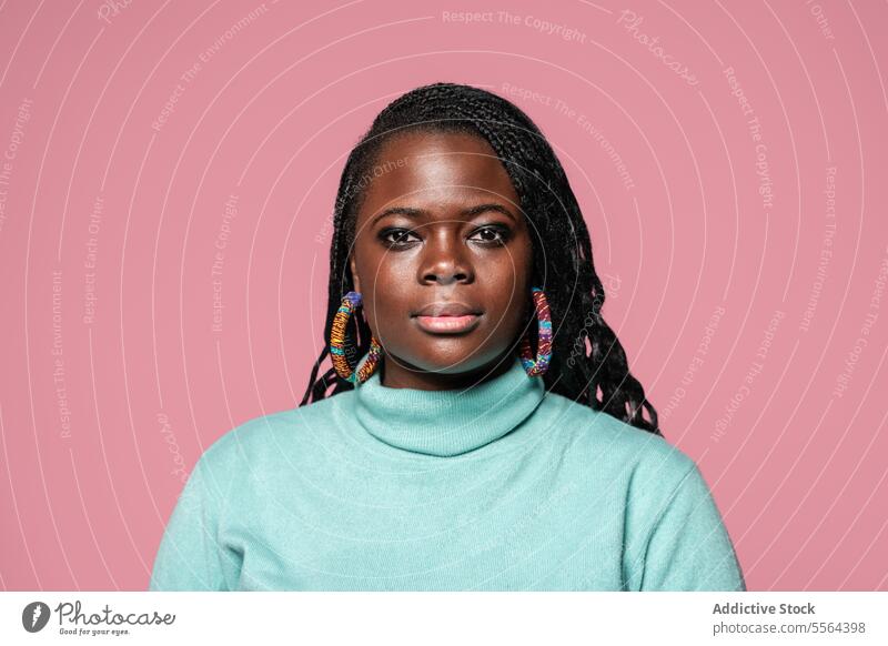 African woman in turquoise turtleneck portrait african braided hair colorful earrings pink background beauty fashion style culture elegance confident gaze