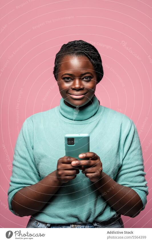 Portrait of smiling woman with smartphone african smile teal sweater pink background cheerful hold joy communication mobile technology modern fashion style