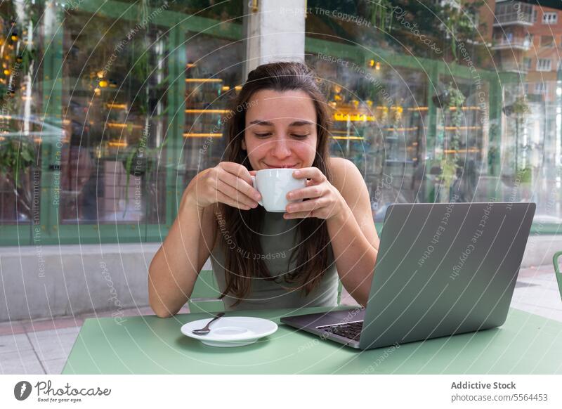Young freelancer drinking hot coffee in cafe woman remote work laptop happy gadget young table hot drink smile female people internet computer entrepreneur