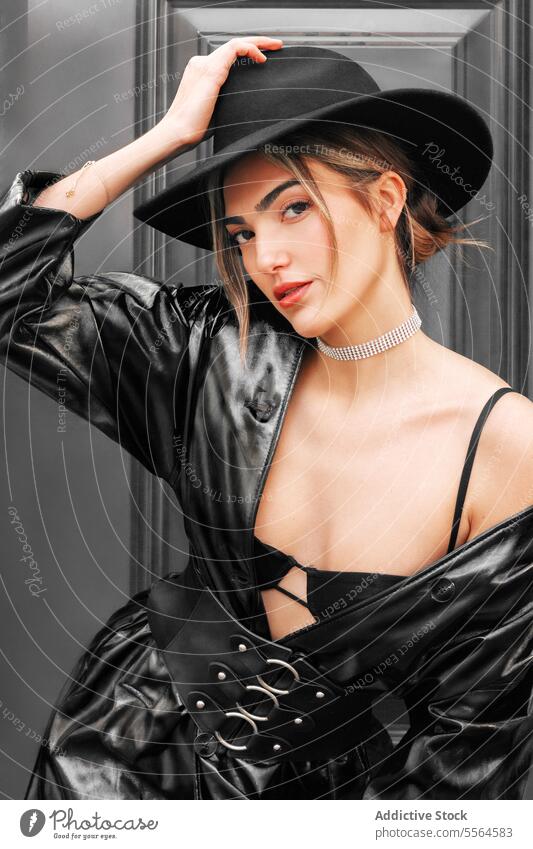 Portrait of a young stylish caucasian woman in a black leather coat and hat looking at the camera. girl model posing fashion dark door close up style portrait