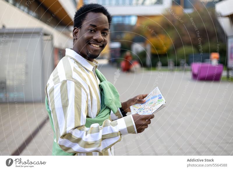 Cheerful black young man standing with map on paved road in daytime building happy smile city cheerful male ethnic african american street guy town outside