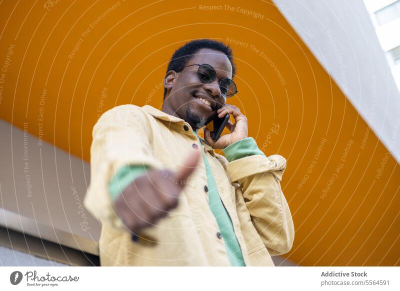 Happy young black man in sunglasses speaking on smartphone and showing thumb up smile building gesture ceiling happy conversation male african american ethnic