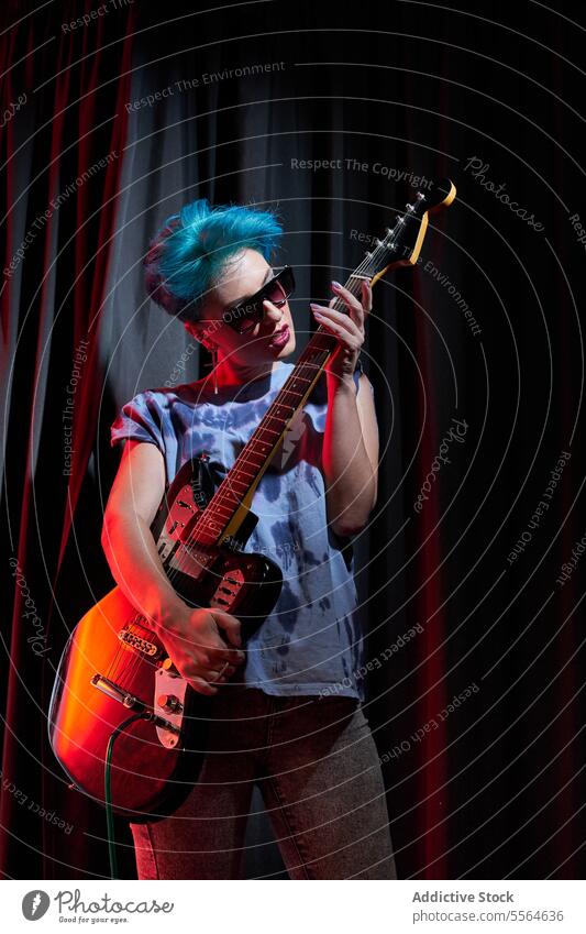 Young stylish woman carrying electric guitar in the hands in dark room musician serious guitarist instrument perform stage portrait dyed hair young female