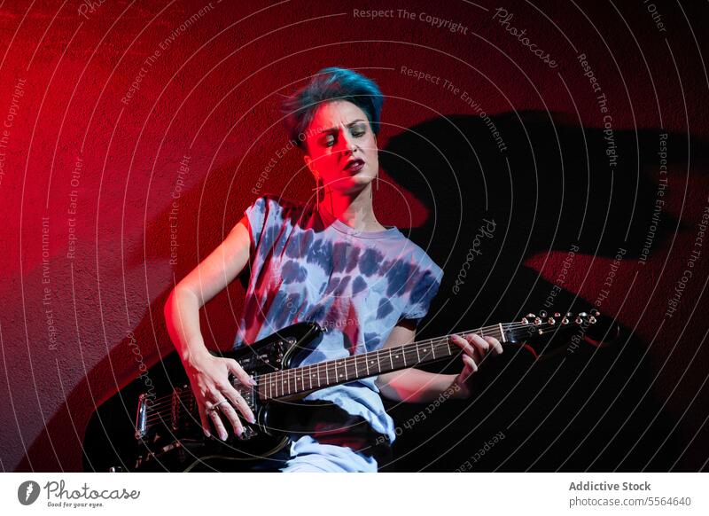 Young stylish woman playing guitar over dark red background in studio musician perform style instrument thoughtful guitarist young female makeup talent melody