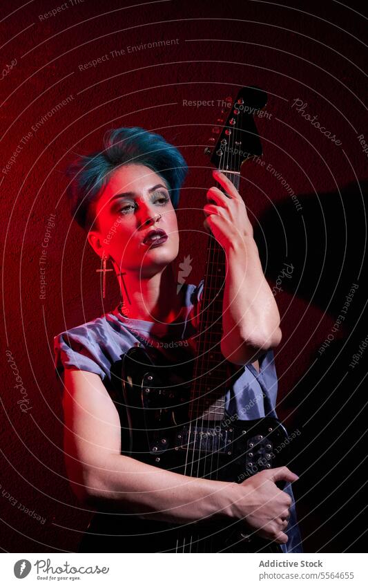 Young stylish woman playing guitar over dark red background in studio musician perform style instrument thoughtful guitarist young female makeup talent melody