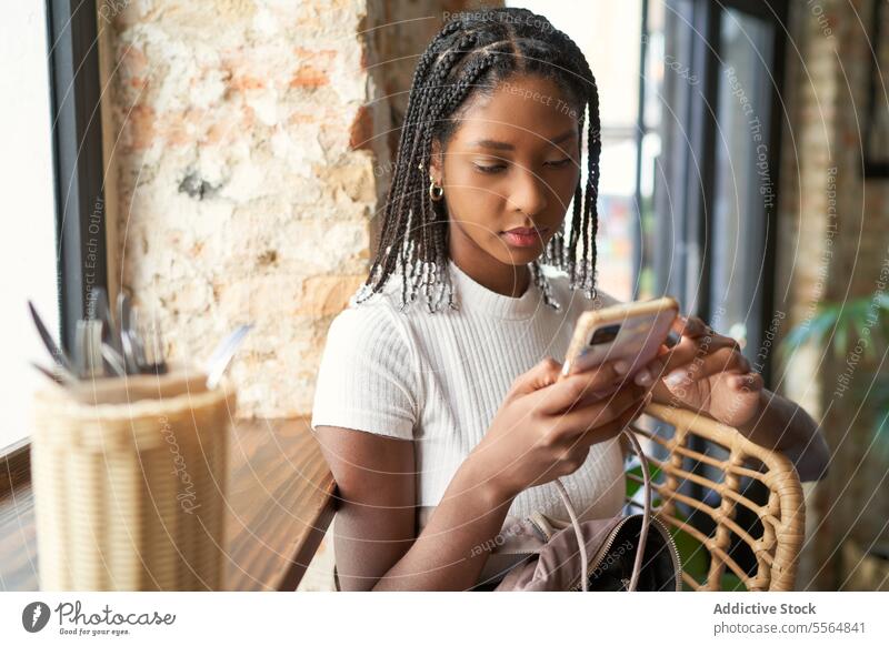 Focused African American woman with afro braids using smartphone browsing pensive concentrate old shabby surfing mobile street basket building serious focus