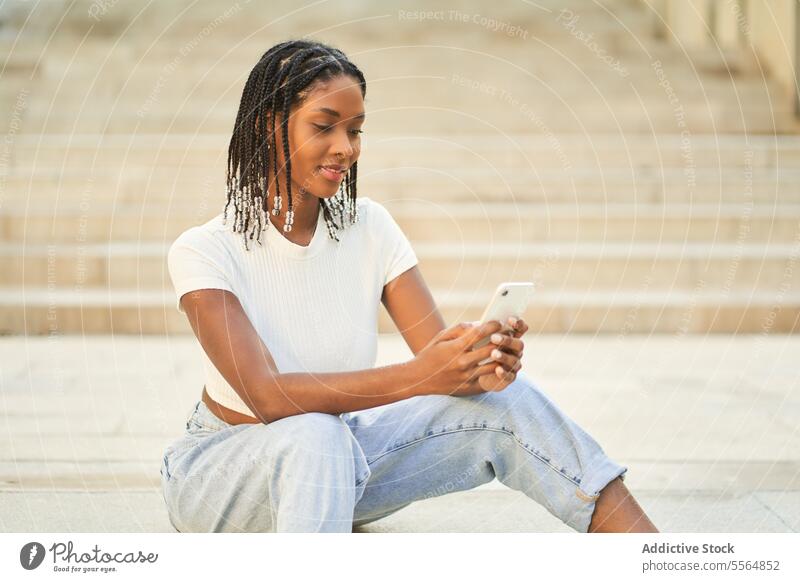 Young ethnic woman browsing mobile phone while sitting on stairs smartphone using staircase happy surfing smile step stairway connection cellphone positive
